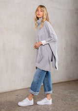 [Color: Light Heather Grey] A model wearing a cozy heather grey turtleneck sweater poncho. 