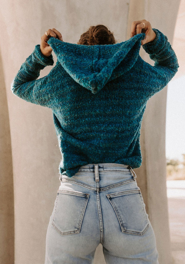 [Color: Teal/Blue] Beautiful model wearing a teal blue and green hooded pullover sweater with drawstring details. Super cute and soft hoodie paired with light wash denim and Ray Ban sunglasses.