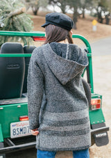[Color: Black/Heather Grey] A woman outside wearing a toggle coat. With two side pockets and a stripe design. 