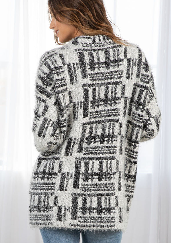 [Color: Silver/Black] A model wearing a fuzzy black and white abstract stripe cardigan sweater. A mid length style featuring long sleeves, side pockets, and an open front.