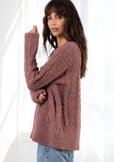 [Color: Vintage Rose] A model wearing a rose pink oversize chunky knit sweater. With contrasting ribbed details and a v neckline.