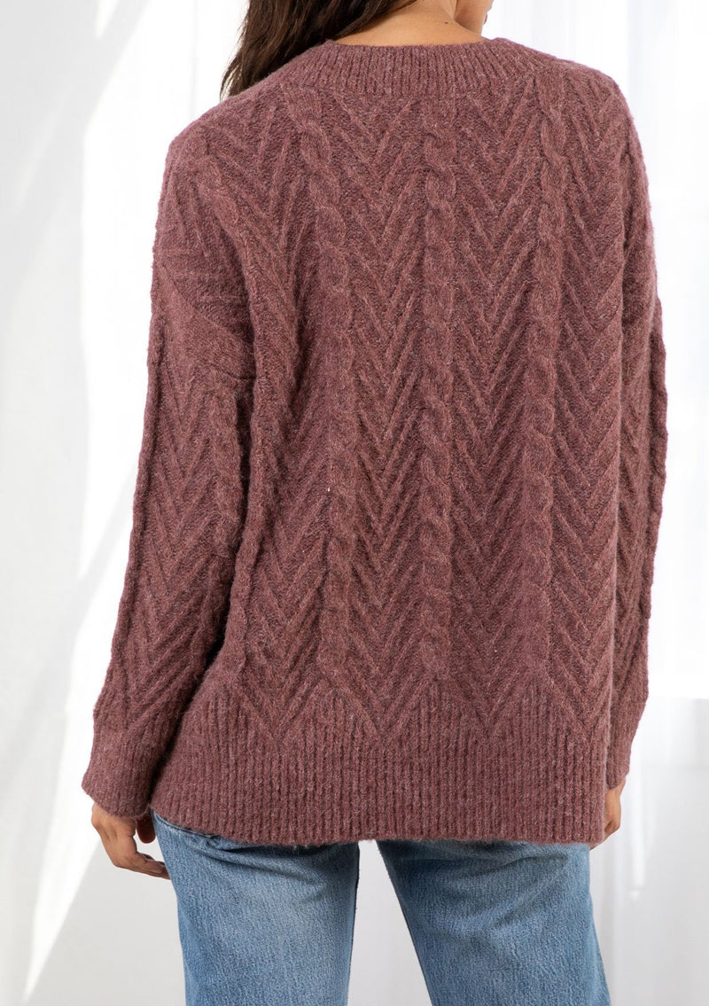 [Color: Vintage Rose] A model wearing a rose pink oversize chunky knit sweater. With contrasting ribbed details and a v neckline.