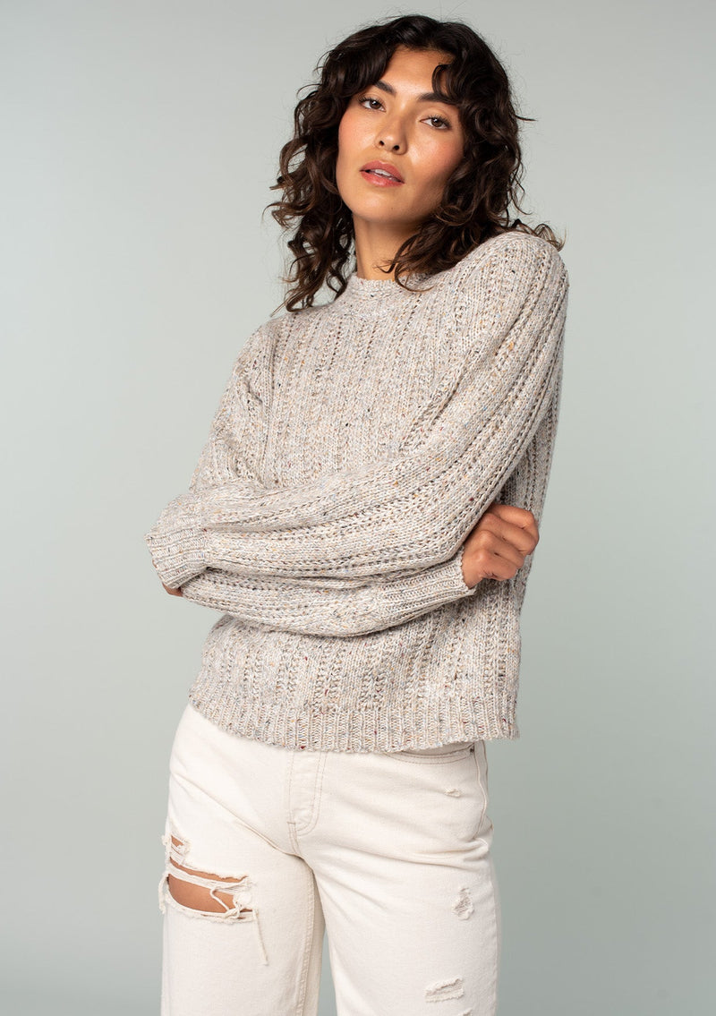 [Color: Oatmeal Multi] A front facing image of a brunette model wearing a perfect vintage style cream colored sweater with modern details. Voluminous long sleeves and a ladder stitch detail add a retro, yet timeless feel to this easy all season layer. Worn here with classic denim. 