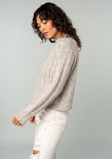 [Color: Oatmeal Multi] A side facing image of a brunette model wearing a perfect vintage style cream colored sweater with modern details. Voluminous long sleeves and a ladder stitch detail add a retro, yet timeless feel to this easy all season layer. Worn here with classic denim. 