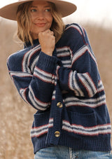 [Color: Navy/Sky] A model wearing a navy blue stripe cardigan sweater. With three oversize buttons, front pockets, and a v neckline. 