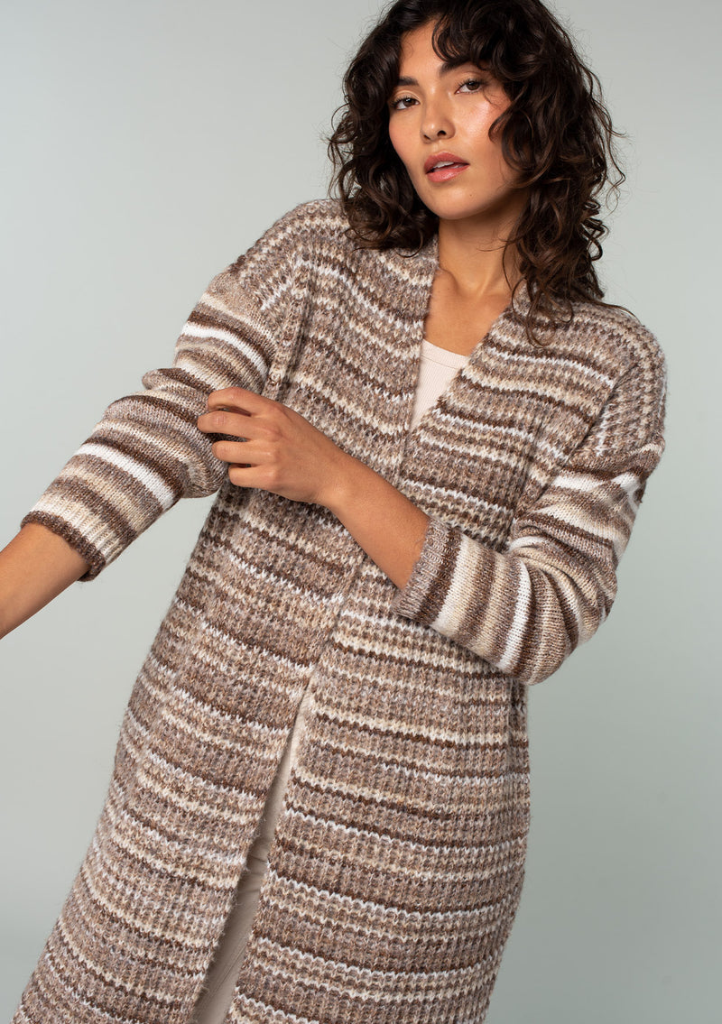 [Color: Brown/Taupe] A close up front facing image of a brunette model wearing a white and brown striped long cardigan. With an open front, contrast striped long sleeves, a shawl collar, and side pockets. 