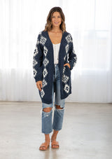 [Color: Indigo/OffWhite] A model wearing an indigo and off white cardigan sweater in a southwestern design. With side pockets, ribbed trim, and a soft chenille fabric. 