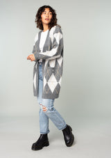 [Color: Charcoal/Grey] A side facing image of a brunette model wearing an ultra soft mid length cardigan in a grey and light grey argyle plaid pattern. With long sleeves, an open front, and side pockets. 