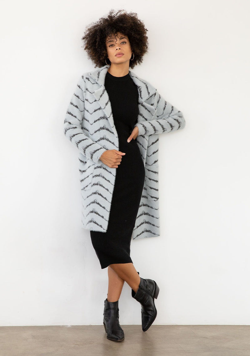[Color: Grey/Charcoal] A model wearing a soft and fuzzy sweater coat in a grey and charcoal chevron design. With a snap button front, side pockets, and a classic notched lapel. 