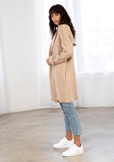 [Color: Taupe/Cream] A model wearing a cozy taupe oversize mid length cardigan. With side pockets, an open front, a shawl collar, and a hoodie. 