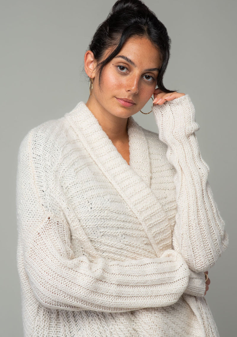 [Color: Oatmeal] A close up front facing image of a brunette model wearing a light oatmeal knit cardigan with a cocoon silhouette, braided cable knit detail, an open front, and a shawl collar. 