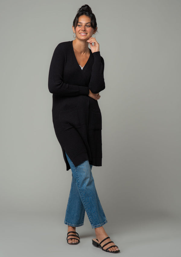 [Color: Black] A front facing image of a brunette model wearing a black waffle knit cardigan. A lightweight mid length cardigan sweater with long sleeves, side pockets, and an open front. 