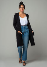 [Color: Black] A full body front facing image of a brunette model wearing a black waffle knit cardigan. A lightweight mid length cardigan sweater with long sleeves, side pockets, and an open front. 