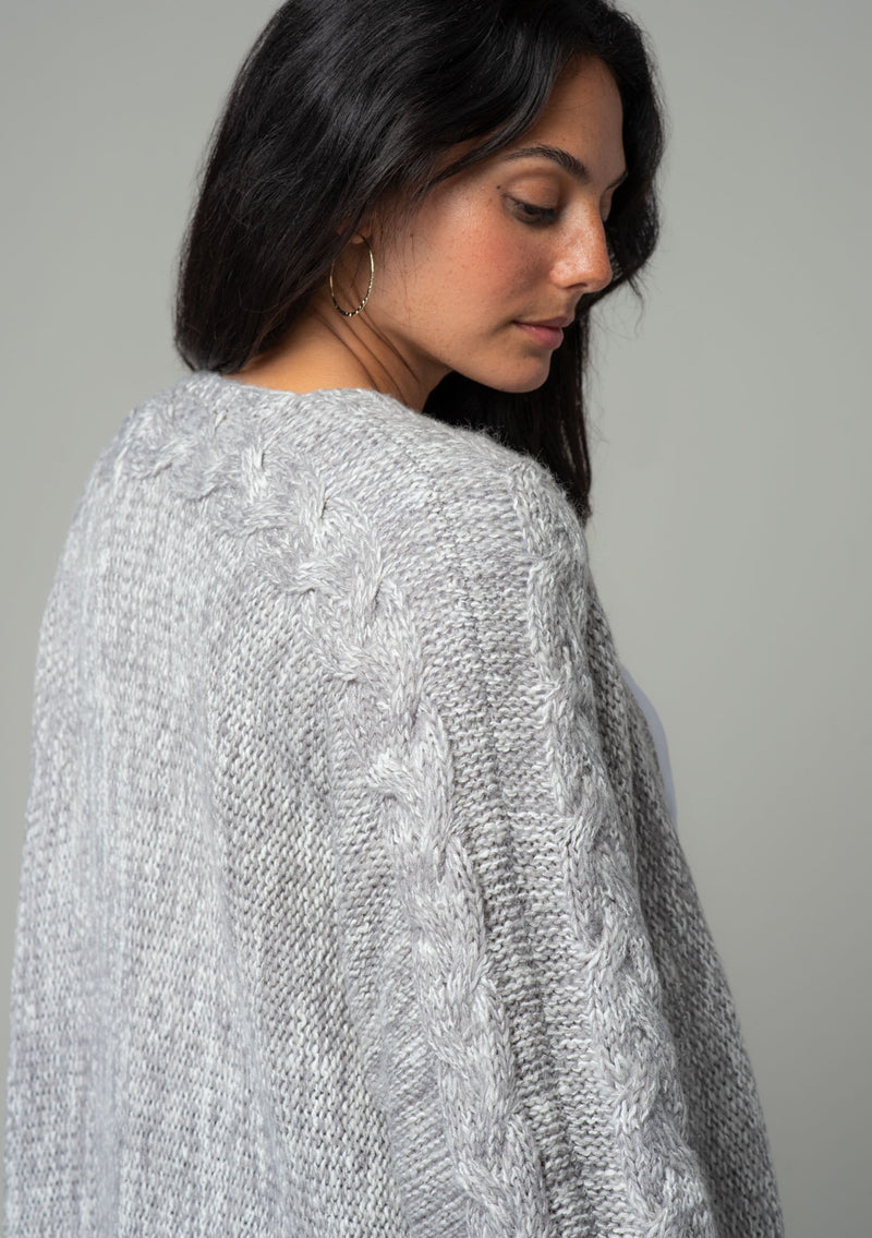 [Color: Heather Grey] A close up back facing image of a brunette model wearing a heather grey chunky knit cardigan. A fall sweater with long sleeves, cable knit sleeve detail, an open front, and side pockets. 