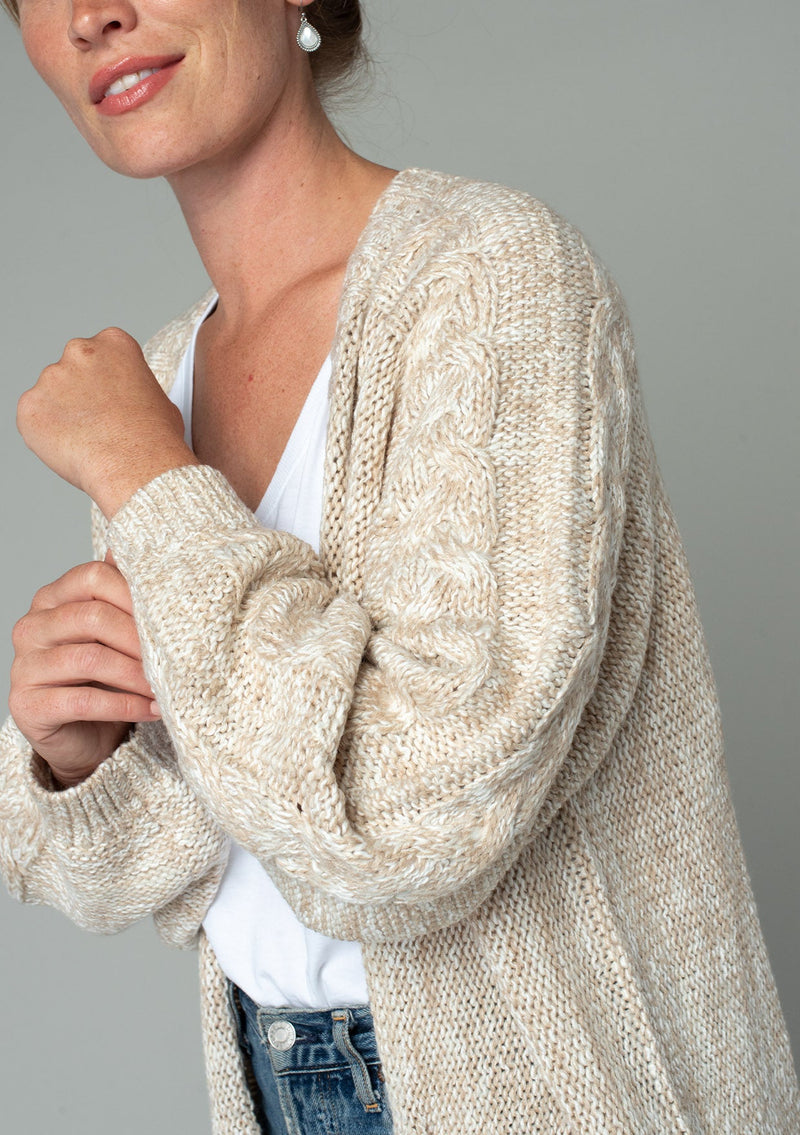 [Color: Oatmeal] A close up side facing image of a red headed model wearing an oatmeal chunky knit cardigan. A fall sweater with long sleeves, cable knit sleeve detail, an open front, and side pockets. 