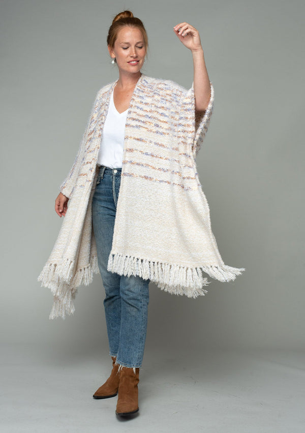 [Color: Oatmeal Multi] A front facing image of a red headed model wearing a fuzzy bohemian sweater poncho in a cream multi color knit. With an open front and tassel fringe trim. 