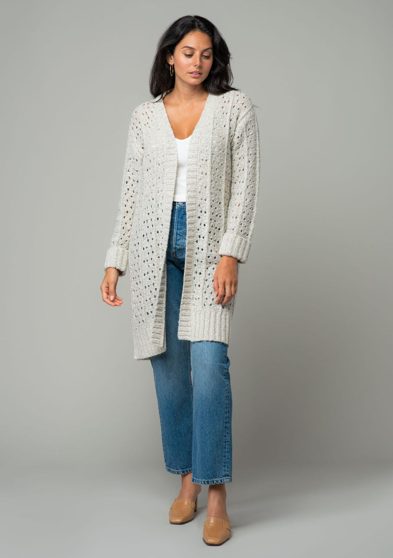 [Color: Oatmeal] A front facing image of a brunette model wearing an oatmeal open knit cardigan sweater. A mid length lightweight cardigan with long sleeves, an open front, and ribbed wrist cuffs. 