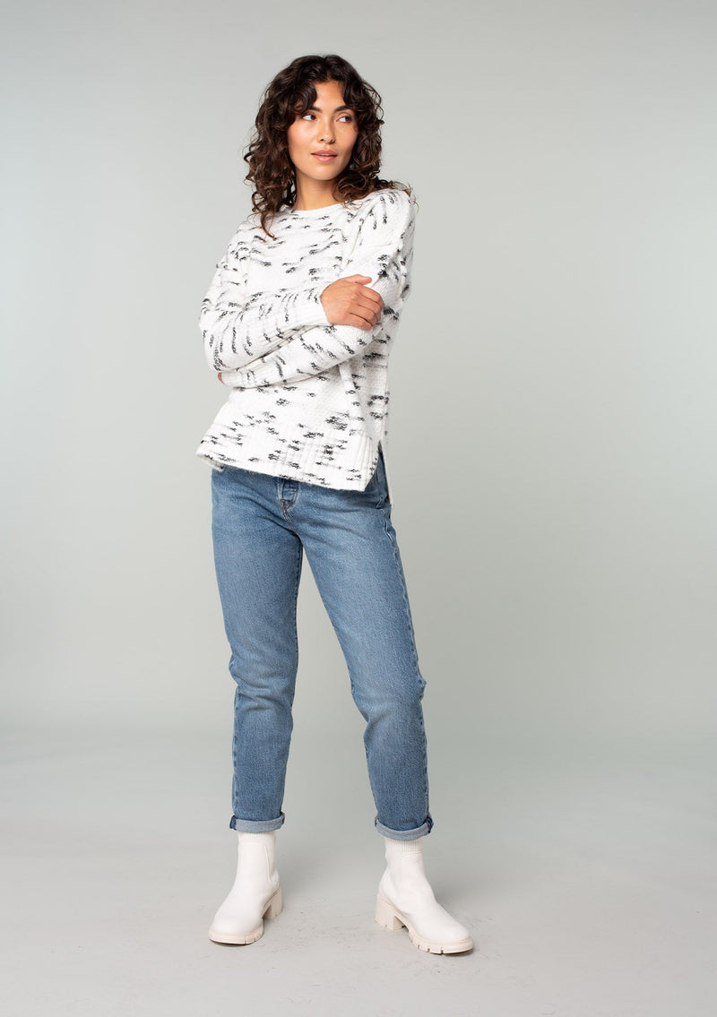 [Color: Ivory/Black] A full body front facing image of a brunette model wearing a black and white speckled knit pullover sweater. With long sleeves, exposed seam details, and a round neckline. 