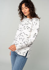[Color: Ivory/Black] A side facing image of a brunette model wearing a black and white speckled knit pullover sweater. With long sleeves, exposed seam details, and a round neckline. 