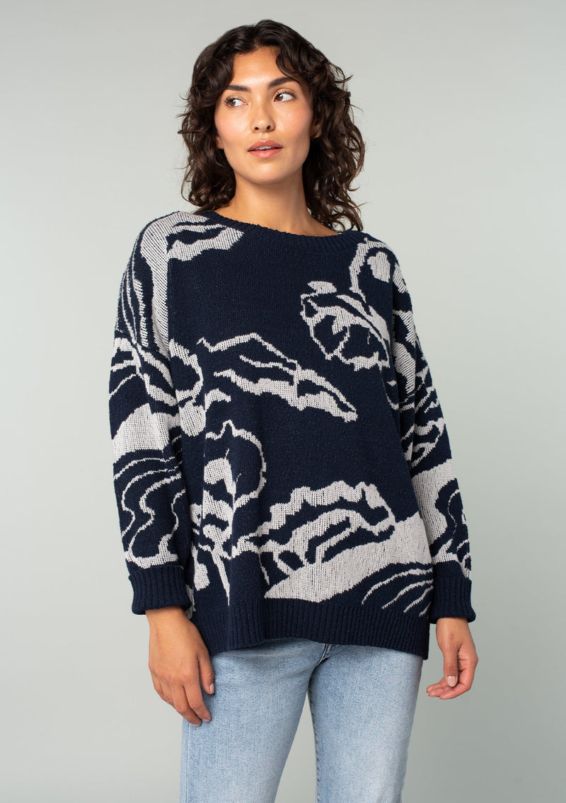 [Color: Navy/Silver] A half body front facing image of a brunette model wearing a bohemian cotton navy sweater with a silver floral motif. With long sleeves and a crew neckline. 