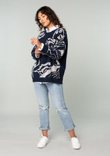 [Color: Navy/Silver] A full body front facing image of a brunette model wearing a bohemian cotton navy sweater with a silver floral motif. With long sleeves and a crew neckline. 