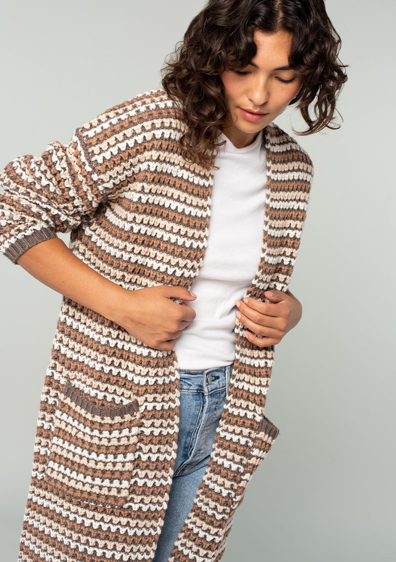 [Color: Mocha Multi] A close up front facing image of a brunette model wearing a brown multi color stripe chunky knit fall cardigan. A long duster cardigan with an open front, long sleeves, and side pockets with contrast trim. 