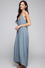 [Color: Slate Blue/Vanilla] A side facing image of a brunette woman wearing a printed light blue v neck maxi dress with a strappy back.