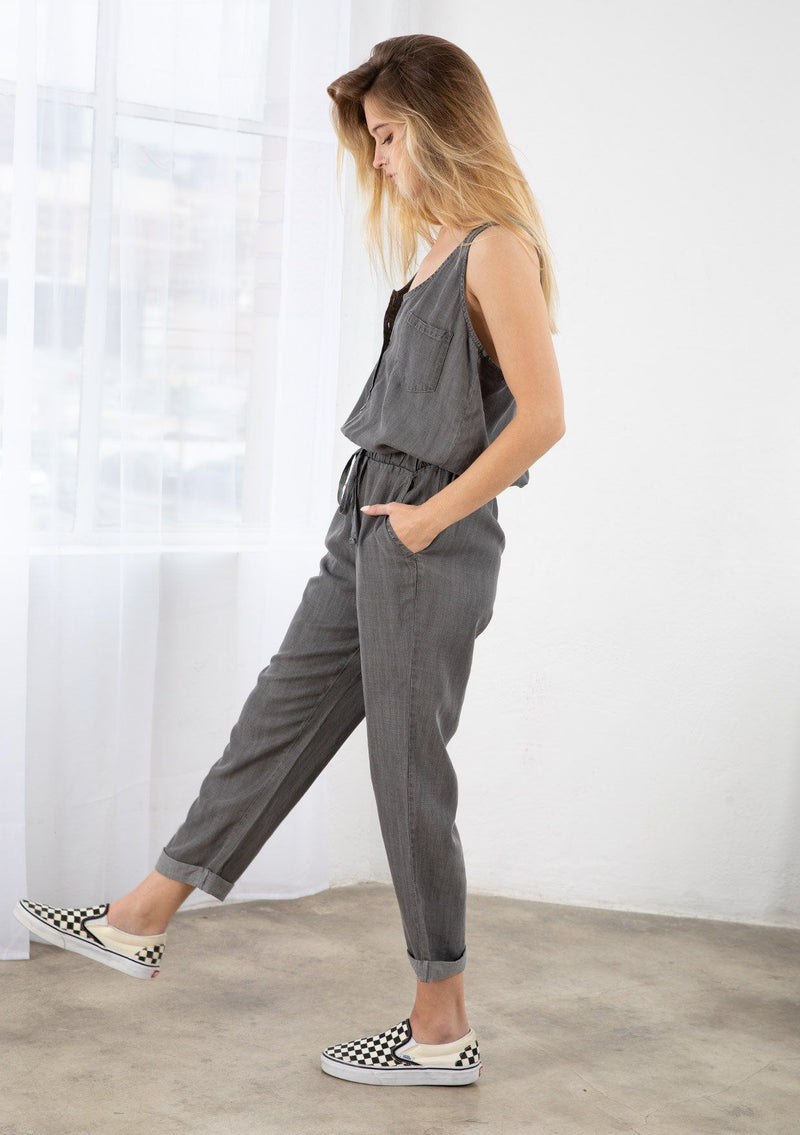 [Color: Ash Wash] A blond model wearing a classic jumpsuit made from eco friendly Tencel. Featuring a wide leg with a cuffed hem, essential side pockets, and a button front.