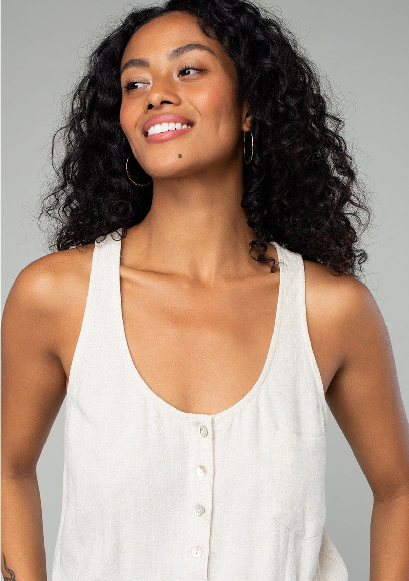 [Color: Natural] A close up front facing image of a brunette model wearing a classic bohemian one piece natural jumpsuit. With a racer back, a button front top, side pockets, a cuffed wide leg, a scoop neckline, and an elastic waist with drawstring. 