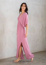 [Color: Smokey Orchid] A model wearing a resort ready light purple maxi dress. With half length kimono sleeves, a plunging v neckline, a smocked elastic empire waist, side slits, and an open back with tie closure.