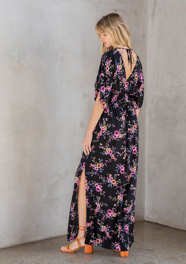 [Color: Black/Wine] A model wearing a gorgeous black and pink floral print resort maxi dress with kimono sleeves, side slits, smocked elastic waist and open back. 