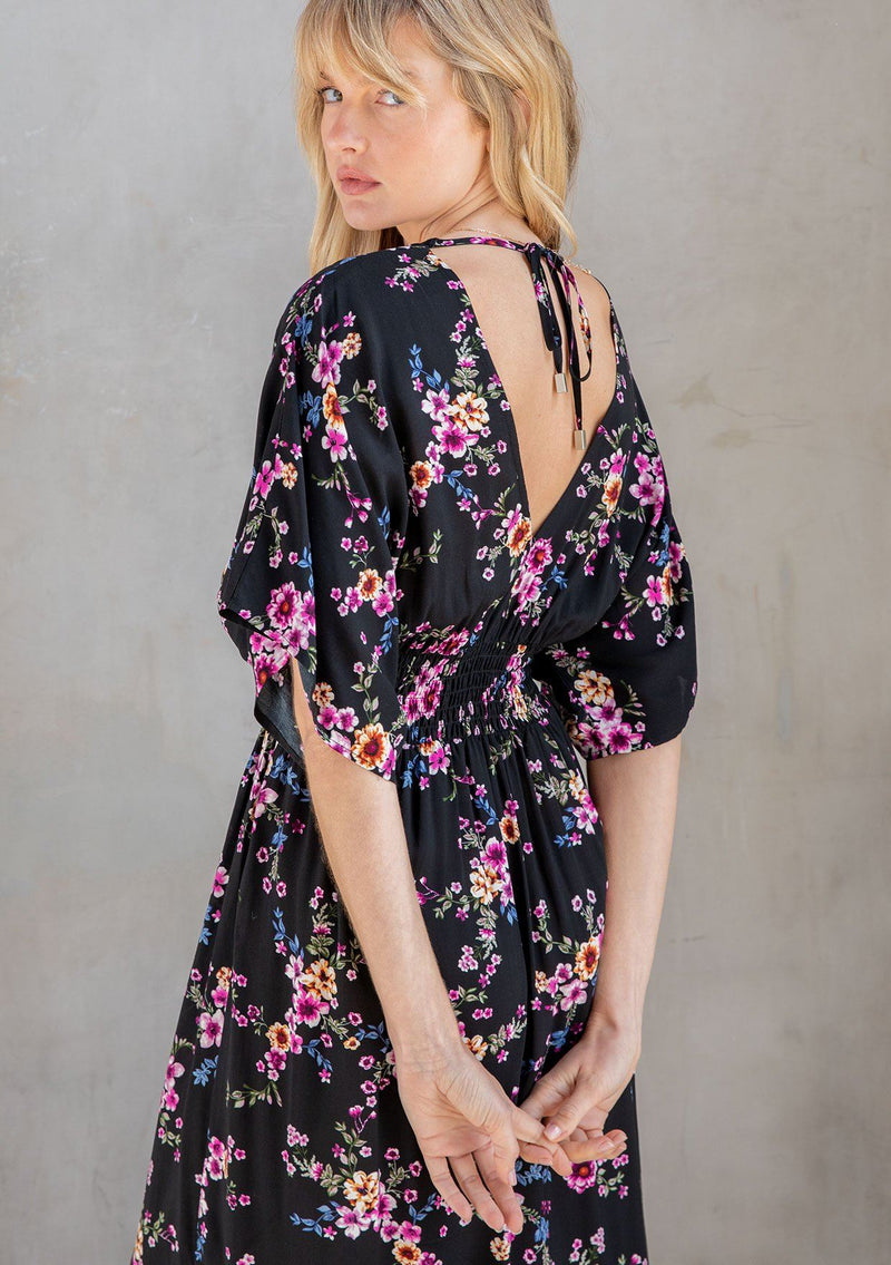 [Color: Black/Wine] A model wearing a gorgeous black and pink floral print resort maxi dress with kimono sleeves, side slits, smocked elastic waist and open back. 