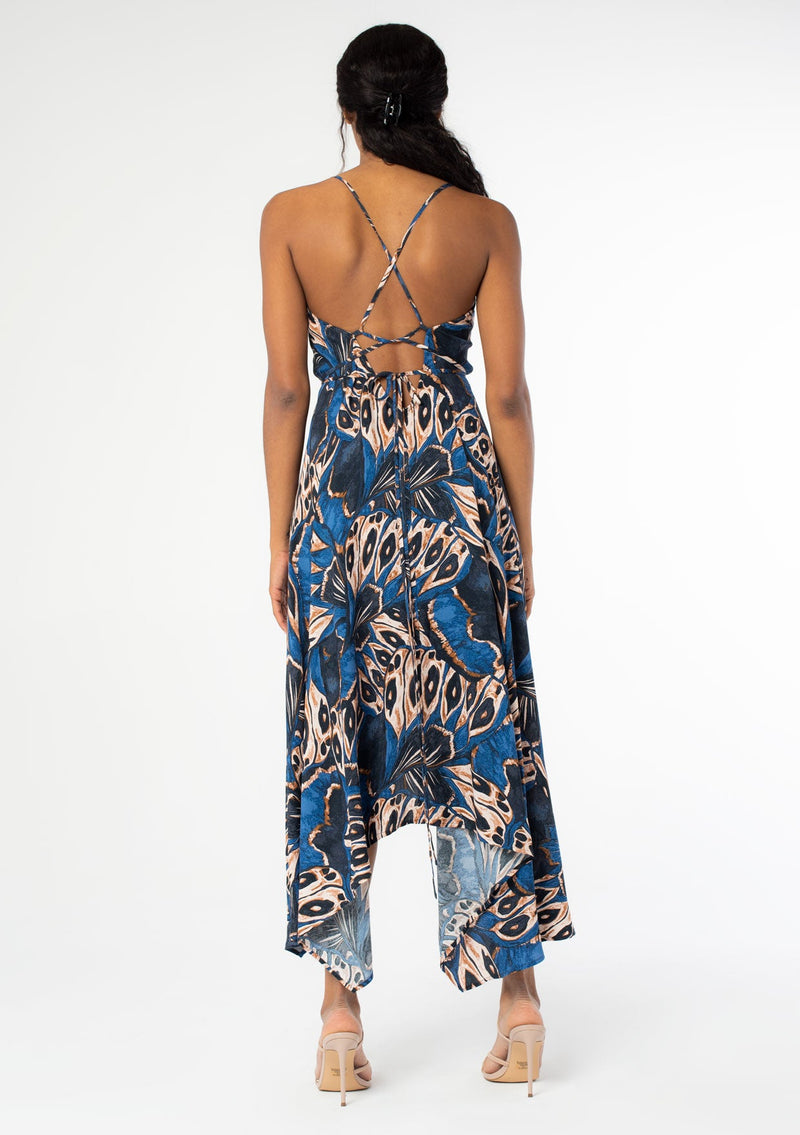 [Color: Cobalt/Tan] A back facing image of a black model wearing a blue and tan butterfly wing print mid length halter dress with long straps that can be tied multiple ways. 