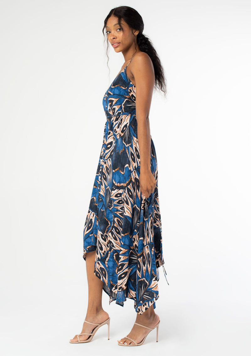 [Color: Cobalt/Tan] A side facing image of a black model wearing a blue and tan butterfly wing print mid length halter dress with long straps that can be tied multiple ways. 