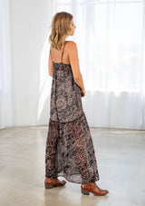 [Color: Black/Mocha] A side facing image of a blonde model wearing a brow and black printed chiffon maxi dress with a scoop neckline and spaghetti straps. 