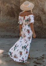 [Color: Vanilla Combo] A woman on the beach wearing an off shoulder floral print maxi dress. Featuring a front slit, short flutter sleeves, and a tie halter neck that can be tied multiple ways.