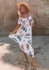 [Color: Vanilla Combo] A woman on the beach wearing an off shoulder floral print maxi dress. Featuring a front slit, short flutter sleeves, and a tie halter neck that can be tied multiple ways.