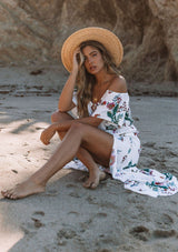 [Color: Vanilla Combo] A woman on the beach wearing an off shoulder floral print maxi dress. Featuring a front slit, short flutter sleeves, and a tie halter neck that can be tied multiple ways.