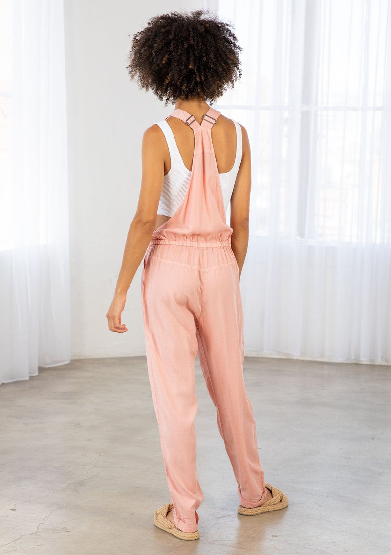 [Color: Blush] A model wearing a lightweight pink overall. Featuring a flattering drawstring waist. The perfect Fall overalls for layering or romping around.