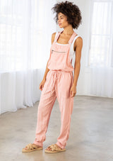 [Color: Blush] A model wearing a lightweight pink overall. Featuring a flattering drawstring waist. The perfect Fall overalls for layering or romping around.