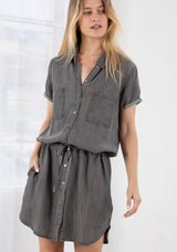 [Color: Ash Wash] A blond model wearing a casual short sleeve shirt dress. Featuring an adjustable drawstring waist for definition, side pockets, and a chic shirttail hemline. 