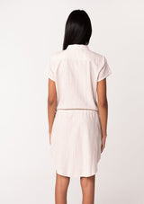[Color: White/Sand] A back facing image of a brunette model wearing a classic mini shirtdress in a white and sand stripe. With short cuffed sleeves, side pockets, a shirttail hemline, a button front, and a drawstring waist.
