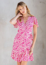 [Color: Natural/Fuchsia] A model wearing a cute and flattering mini wrap dress in a natural and pink abstract circle print. With ruffled hem and flounce sleeve. 