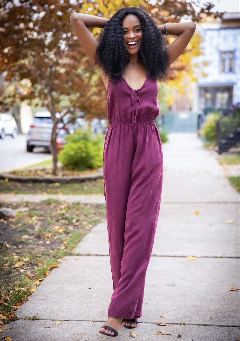 [Color: Burgundy] A woman wearing a one piece jumpsuit. Featuring a wide leg, a front keyhole detail, an elastic cinched waist, and side pockets.