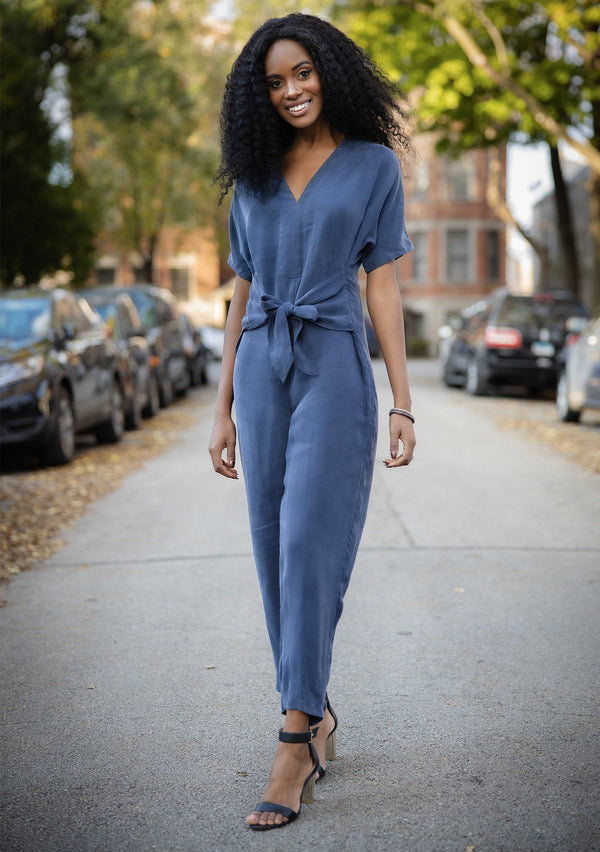[Color: Navy] A short sleeve jumpsuit featuring a waist defining tie front detail, a flirty v back with tie detail, and an easy tapered leg.