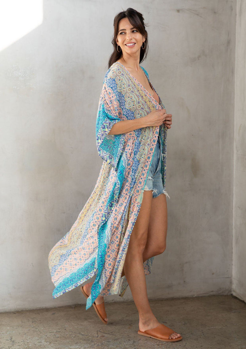 [Color: Turquoise Multi] A model wearing a multi colored paisley print kimono. Featuring a tassel tie closure.