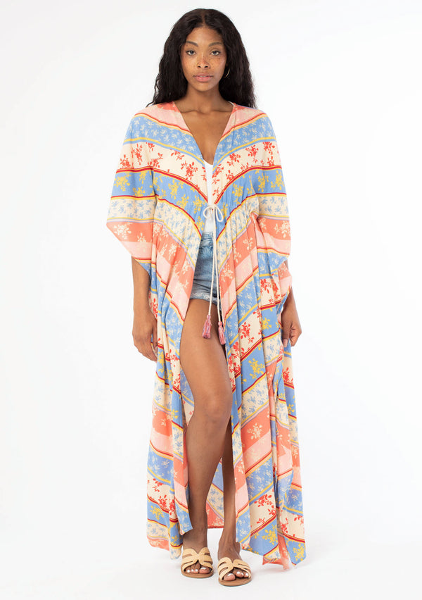 [Color: Indigo/Red] A black model with long dark hair wearing a red and blue chevron floral stripe duster kimono. A maxi length kimono with half length kimono sleeves, side slits, and an adjustable tassel tie front waist. A beach cover up kimono for Spring and Summer. 