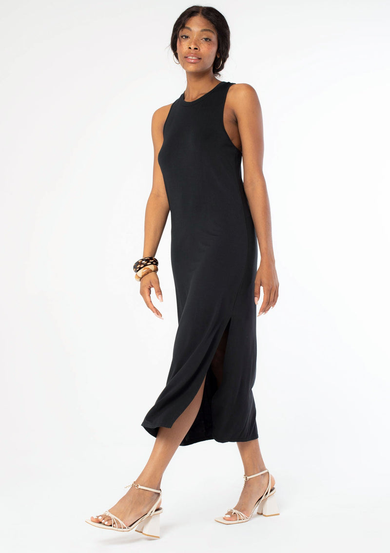 [Color: Black] A side facing image of a black model wearing a soft and stretchy sleeveless black maxi dress. With a round crew neckline, a sexy side slit, a racer back with a knot detail, and a relaxed fit.