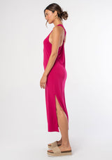 [Color: Mulberry] A model wearing a soft and stretchy sleeveless pink maxi dress. With a round crew neckline, a sexy side slit, a racer back with a knot detail, and a relaxed fit.