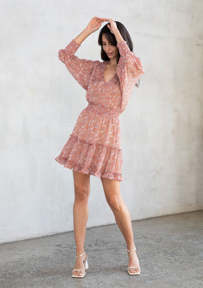 [Color: Coral/Natural] A model wearing a cute bohemian coral paisley chiffon mini dress featuring a smocked elastic waist and a split v neckline with tassel ties. With gold lurex detail.